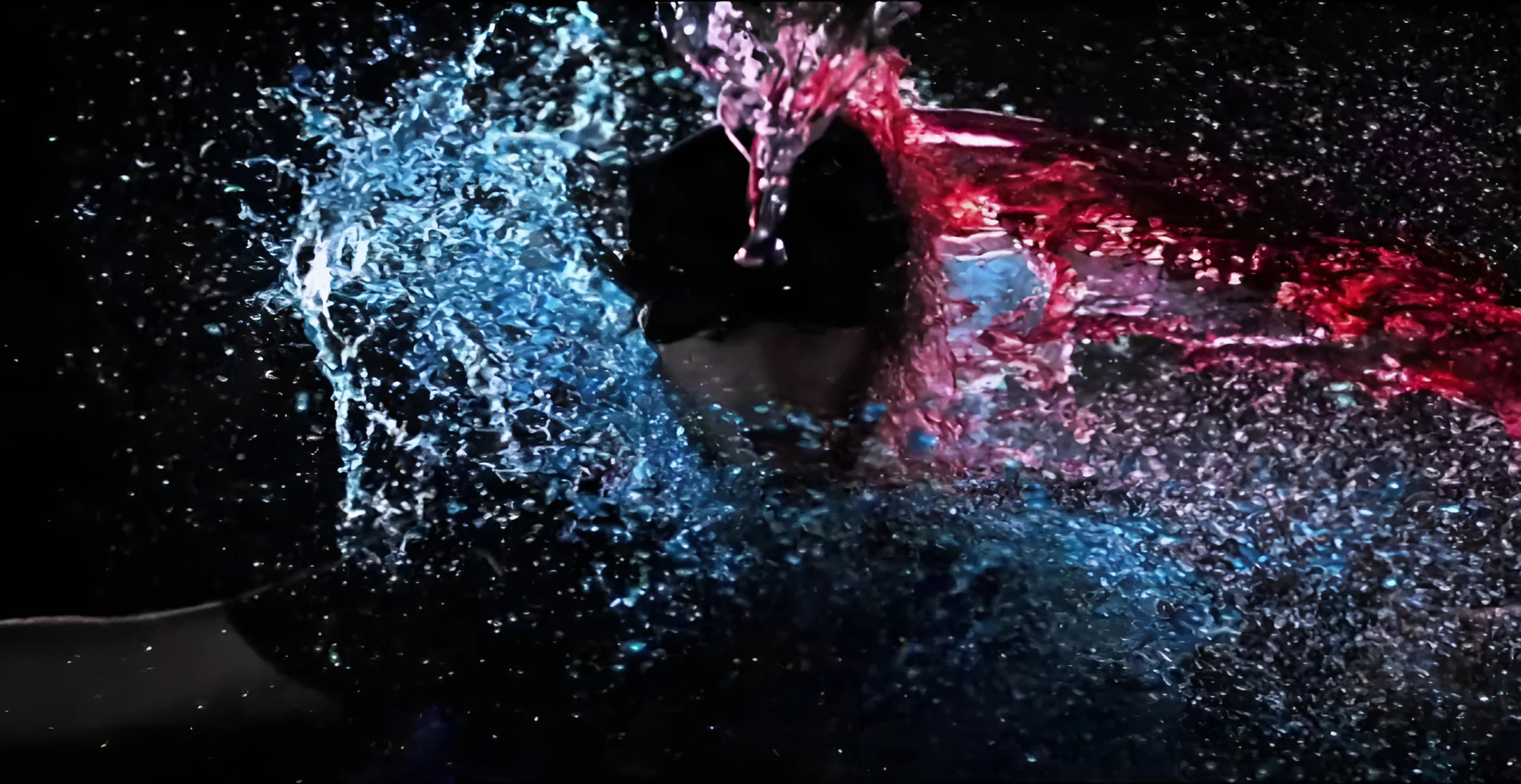 A figure surrounded by splashing water lit in blue and red in the video Scompare.