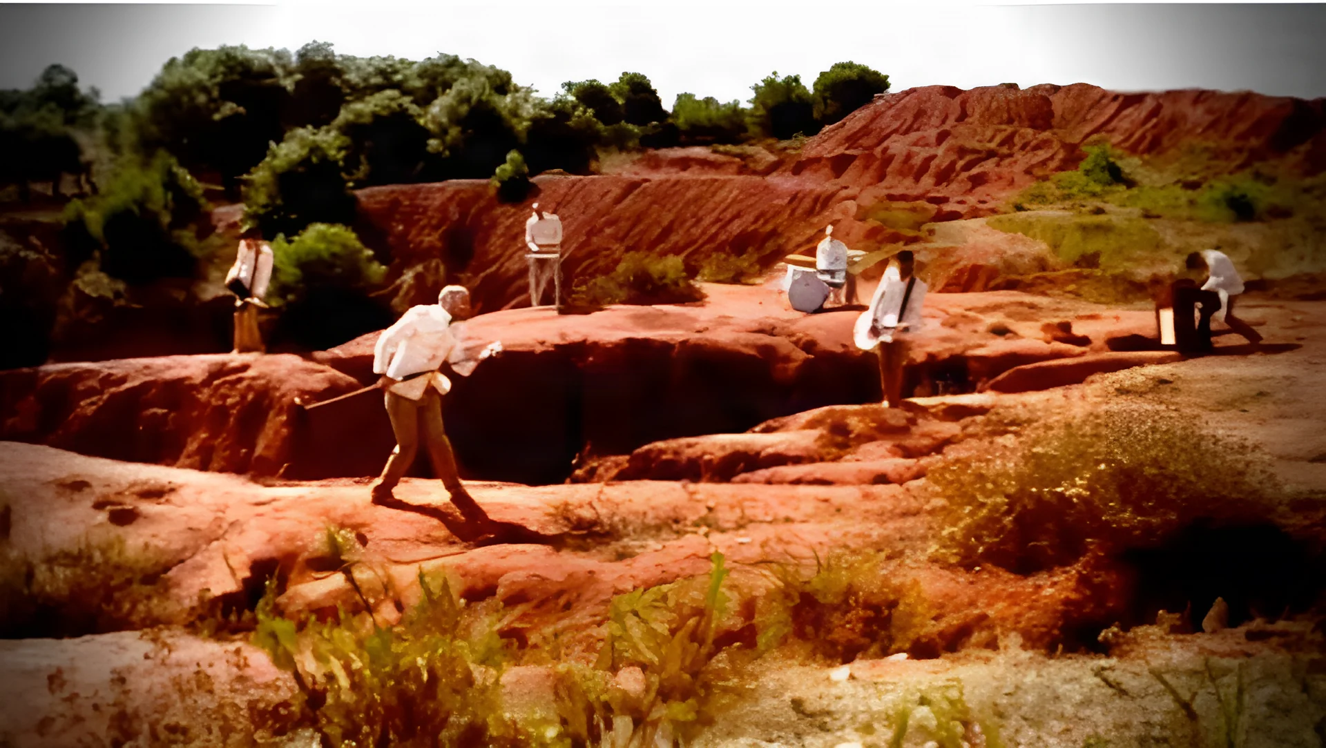 Figures in light-coloured clothing among red rock formations in an open landscape.
