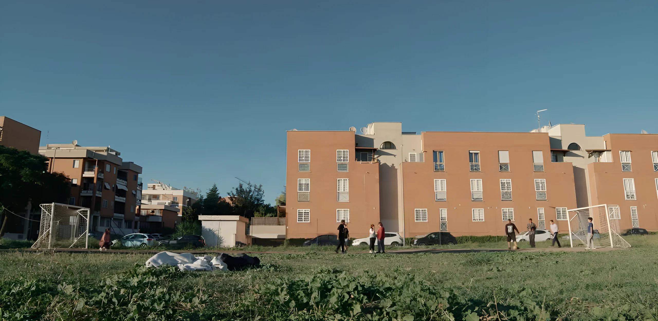 People on a neighbourhood football pitch, with residential buildings in the background, on the cover of La Casa.