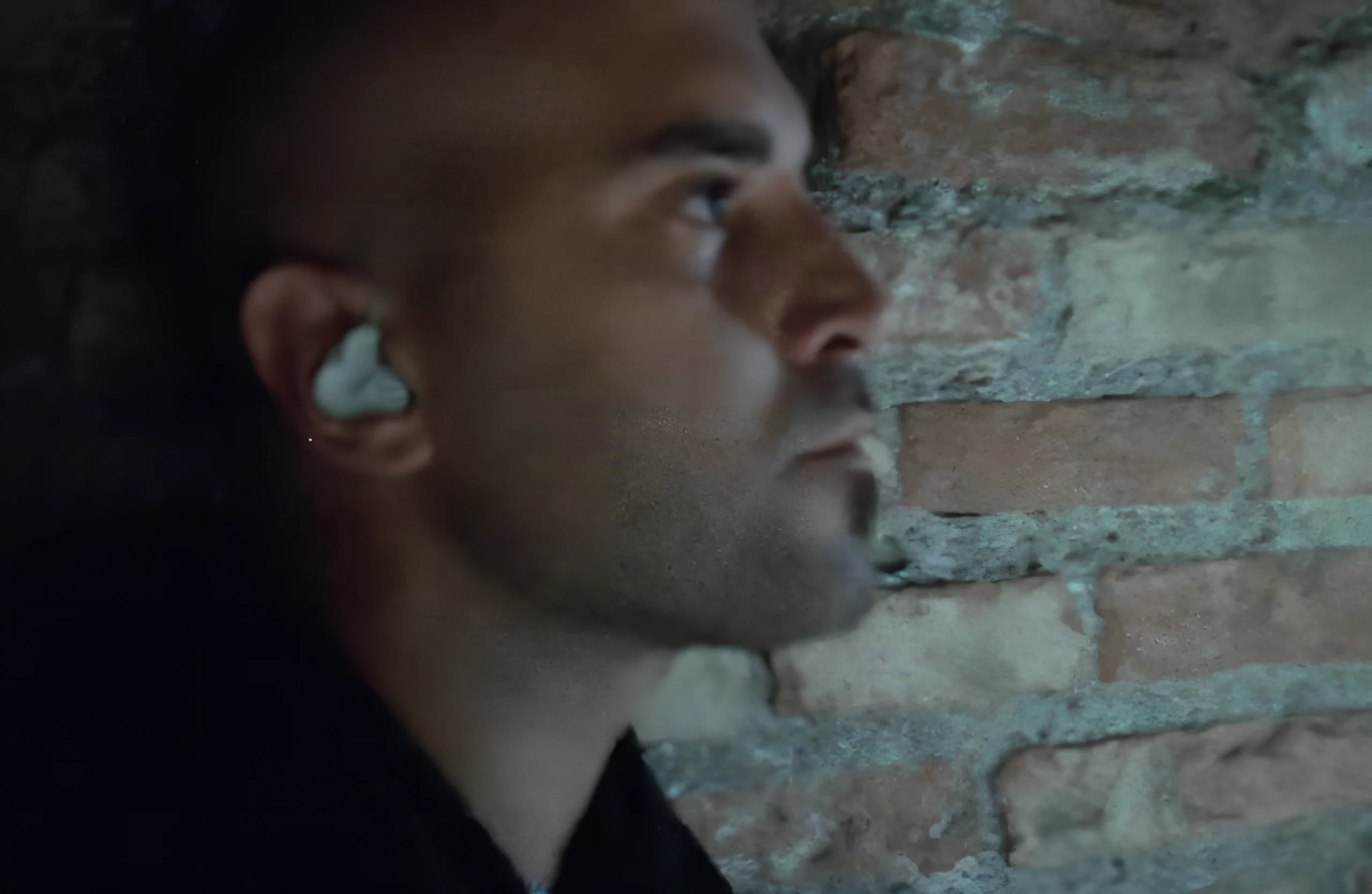 A close-up profile wearing an earpiece, against a brick wall, in a scene from Negramaro — Il film segreto.